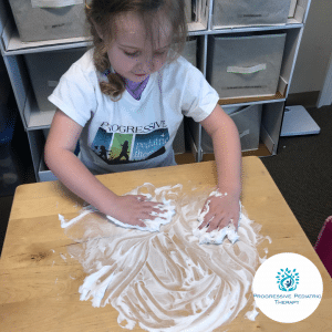 A little girl wearing a progressive shirt is playing with shaving cream