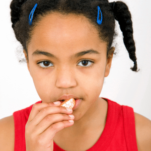 A young girl in a red tank top is eating an orange