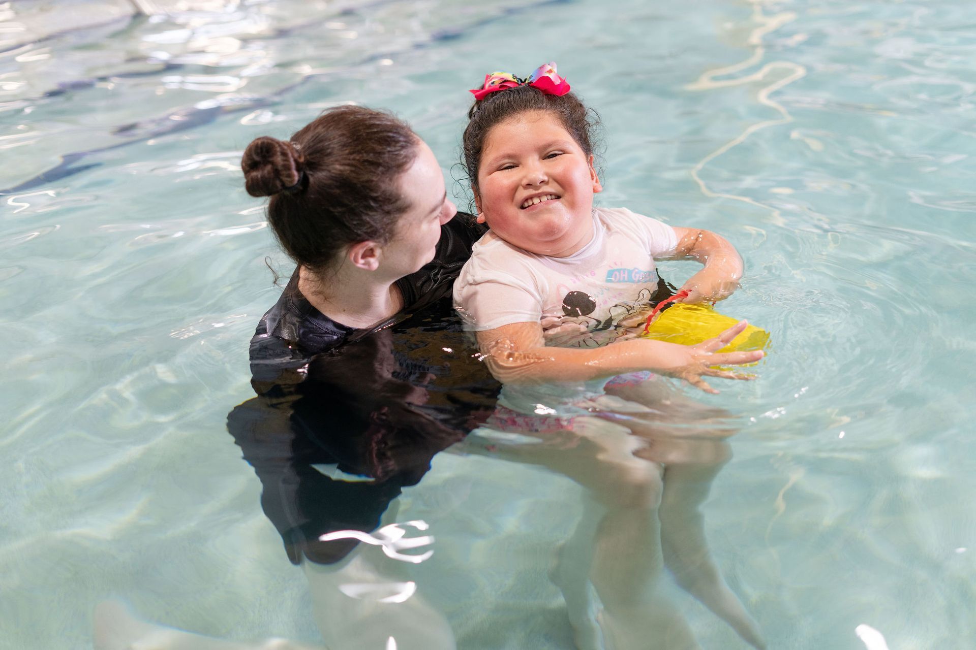 A woman is holding a little girl in a swimming pool.