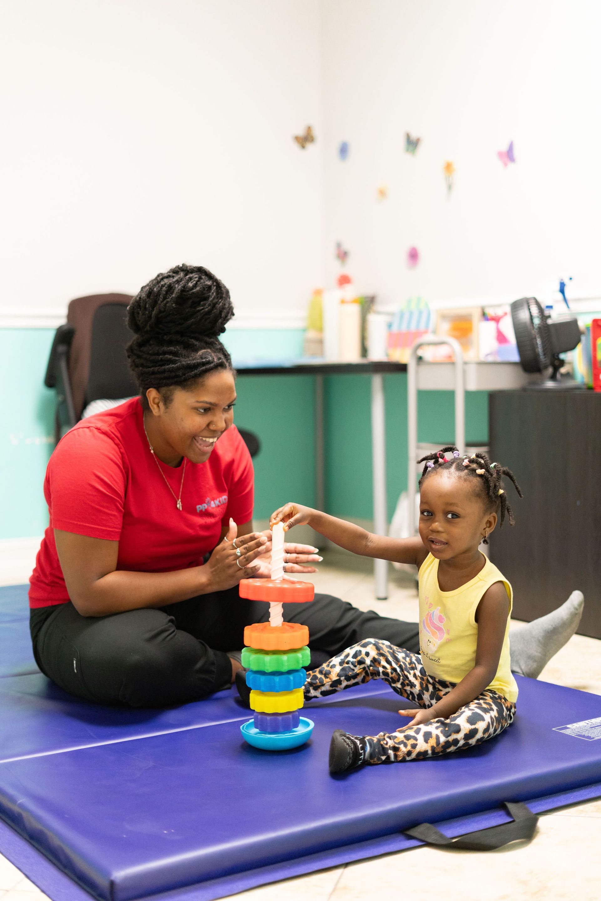 A woman is sitting on a mat playing with a little girl.