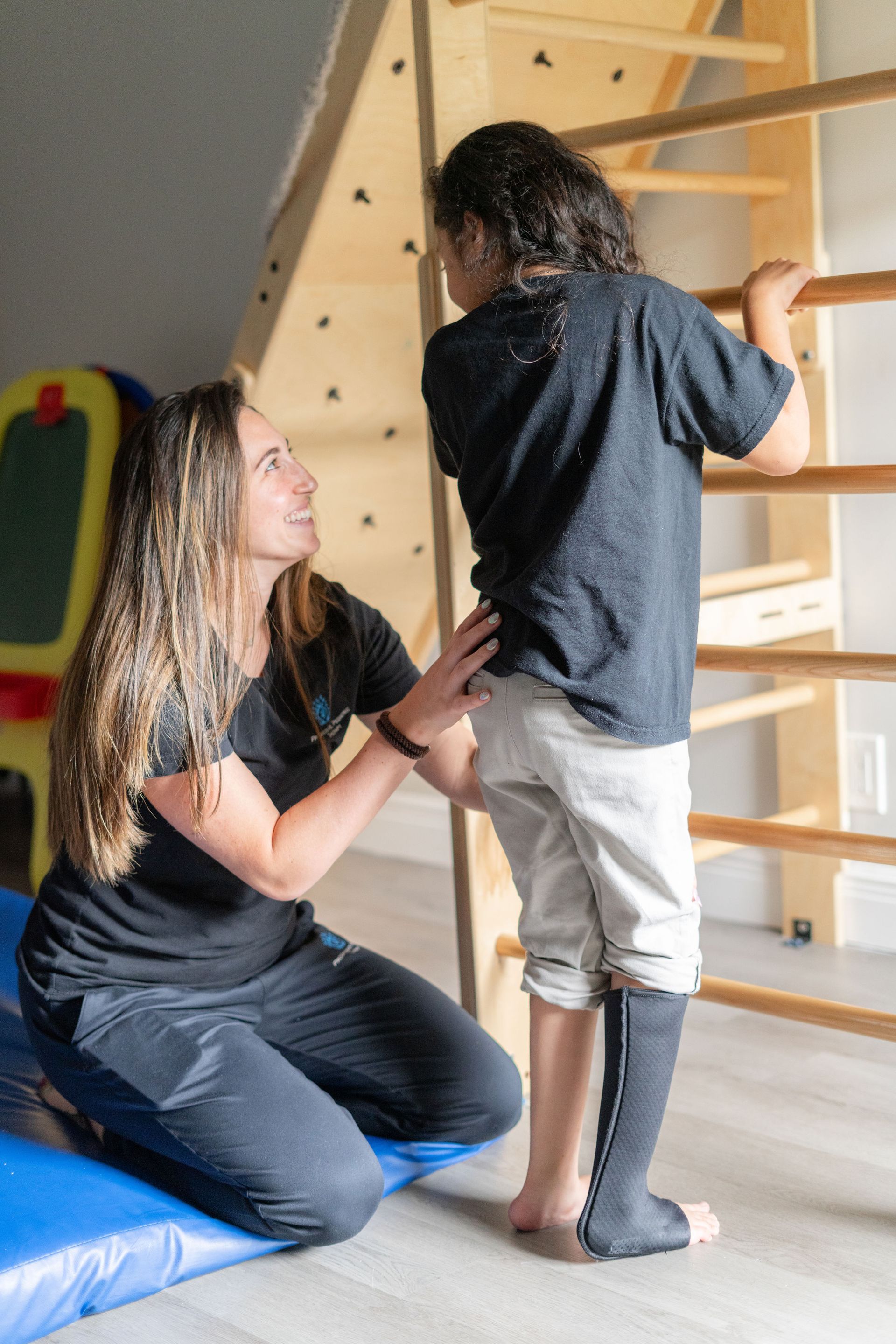 A woman is kneeling down next to a child who is standing on a ladder.