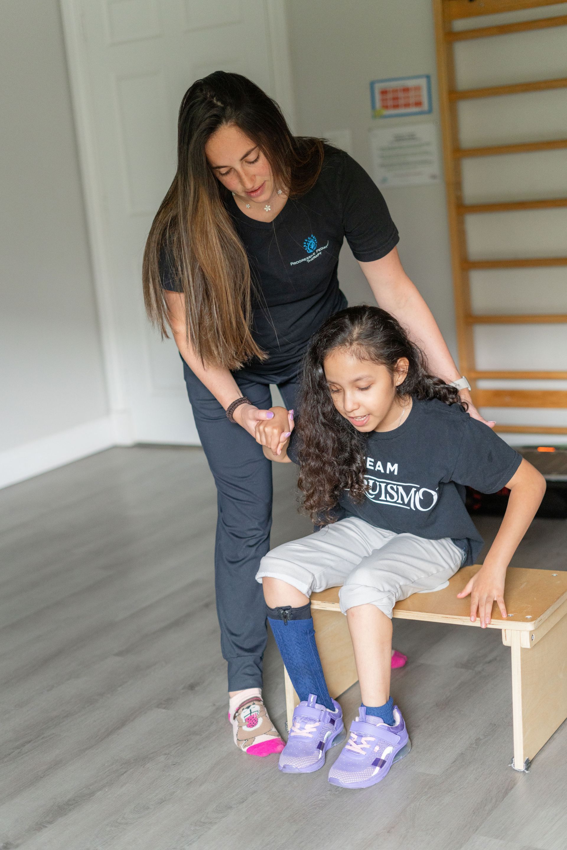 A woman is helping a little girl sit on a wooden bench.