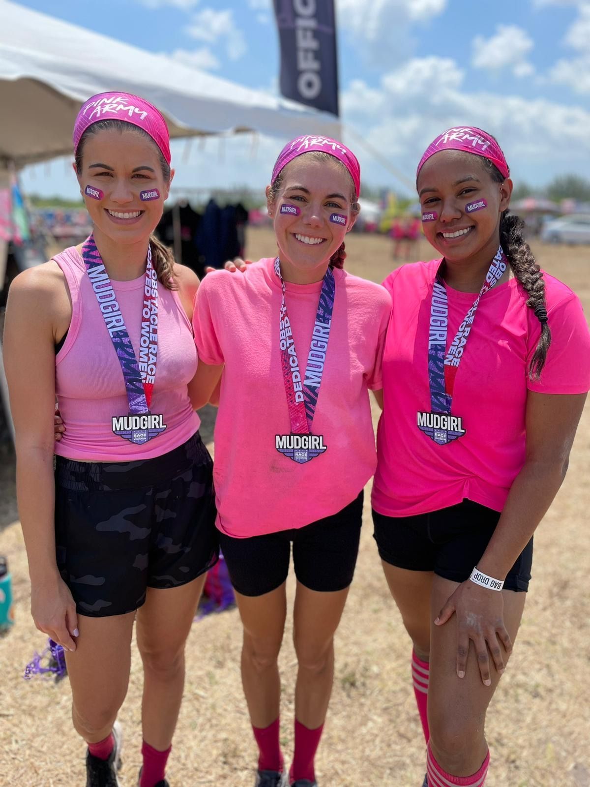 Three women wearing pink shirts and medals are posing for a picture.
