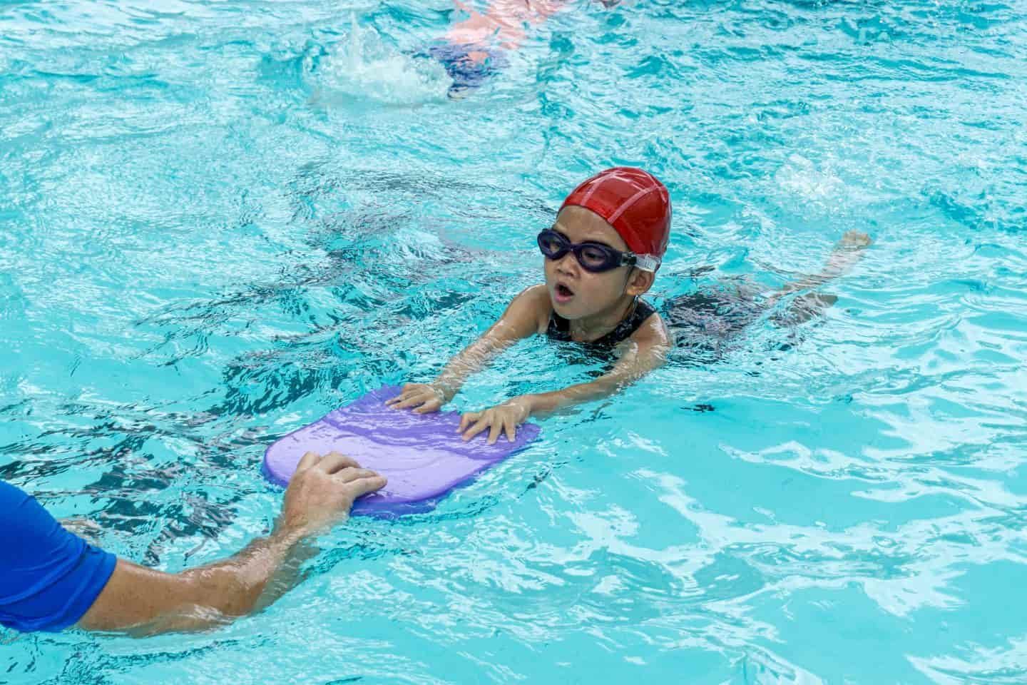 A little girl is swimming in a pool with a purple boogie board.
