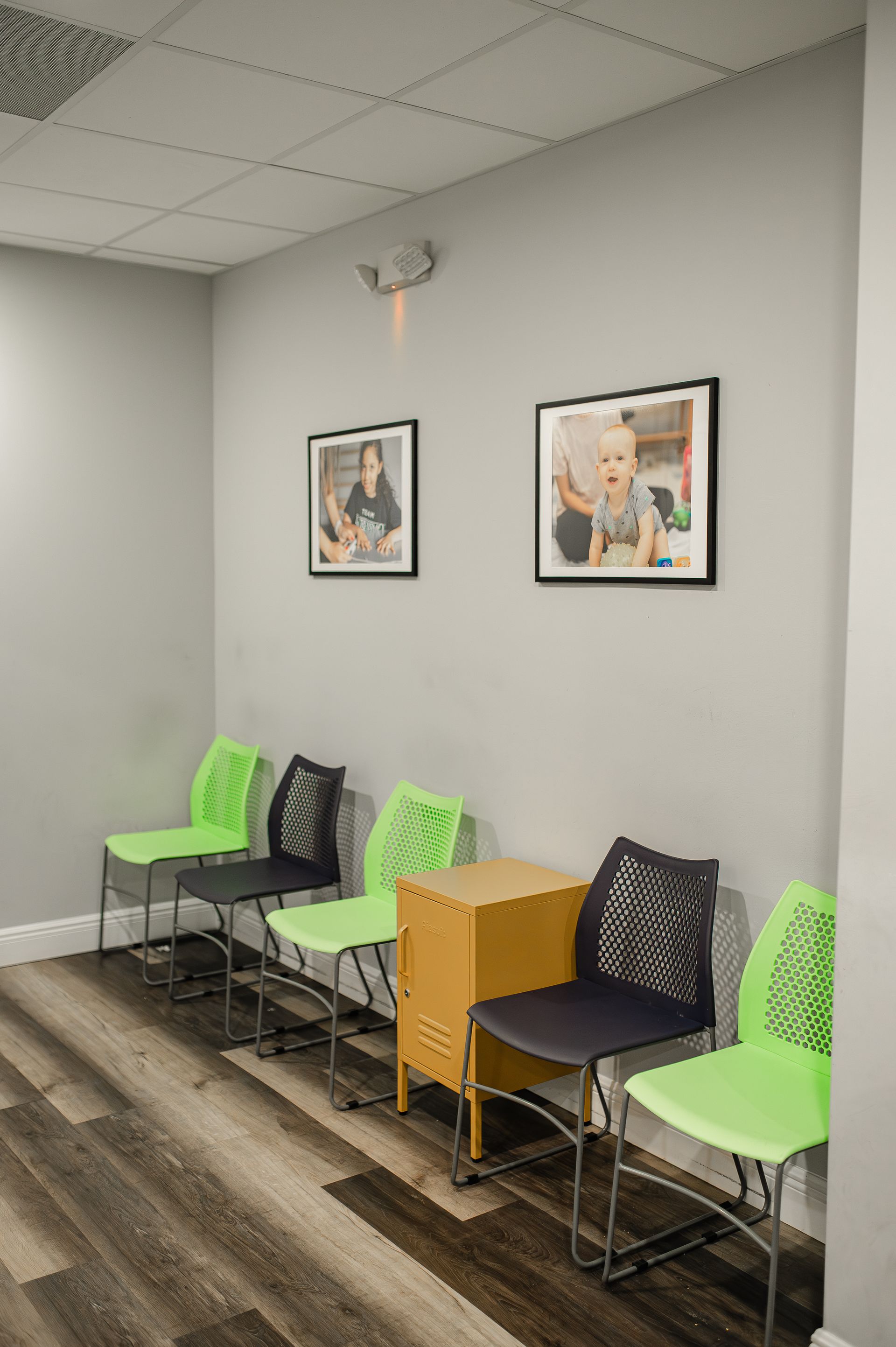 Waiting room with green and black chairs, framed photos, and a small wooden cabinet.