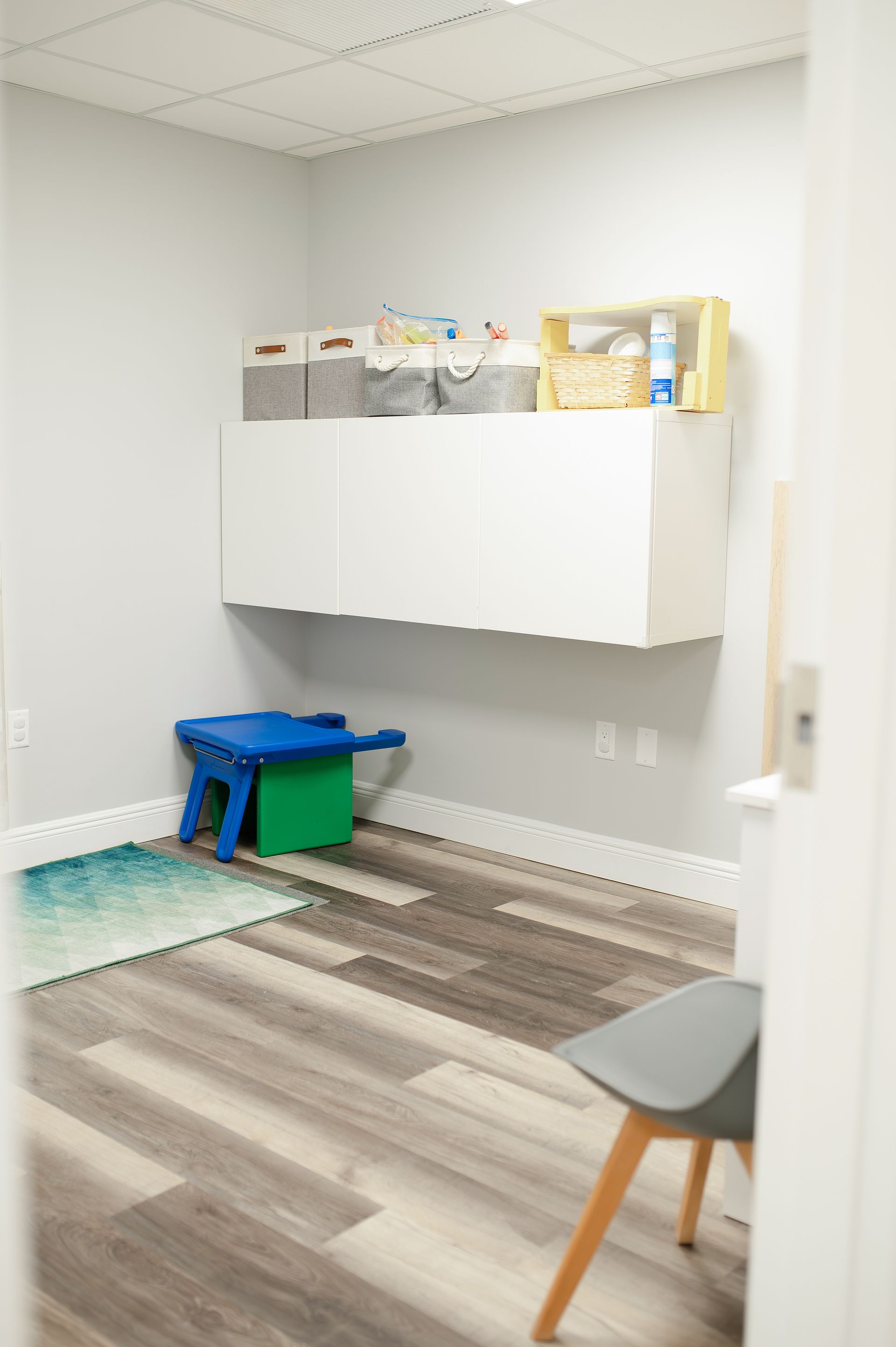 Small, bright waiting room with blue and green rug, floating white cabinet, and a blue stool.