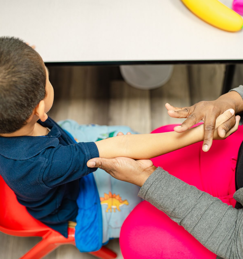 A woman is kneeling down next to a young boy who is standing on a wooden floor