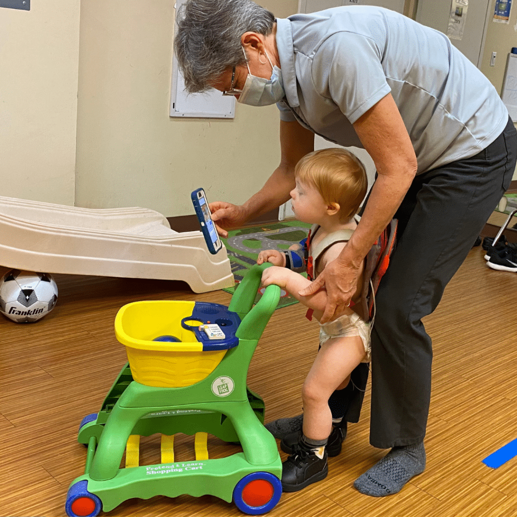 A man wearing a mask is helping a baby push a shopping cart.