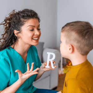 A woman is holding a letter r in front of a young boy.