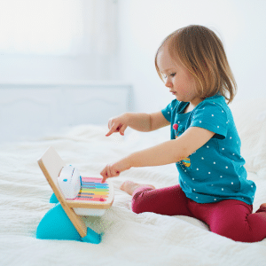 A little girl is sitting on a bed playing with a toy piano.