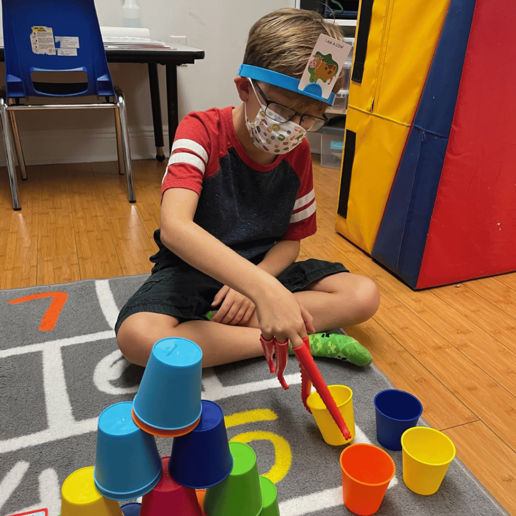 A young boy wearing a mask is playing with cups on the floor.