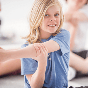 A young girl is sitting on the floor stretching her arms.