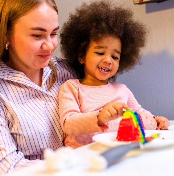 A woman and child are sitting at a table with a rainbow cake on a plate