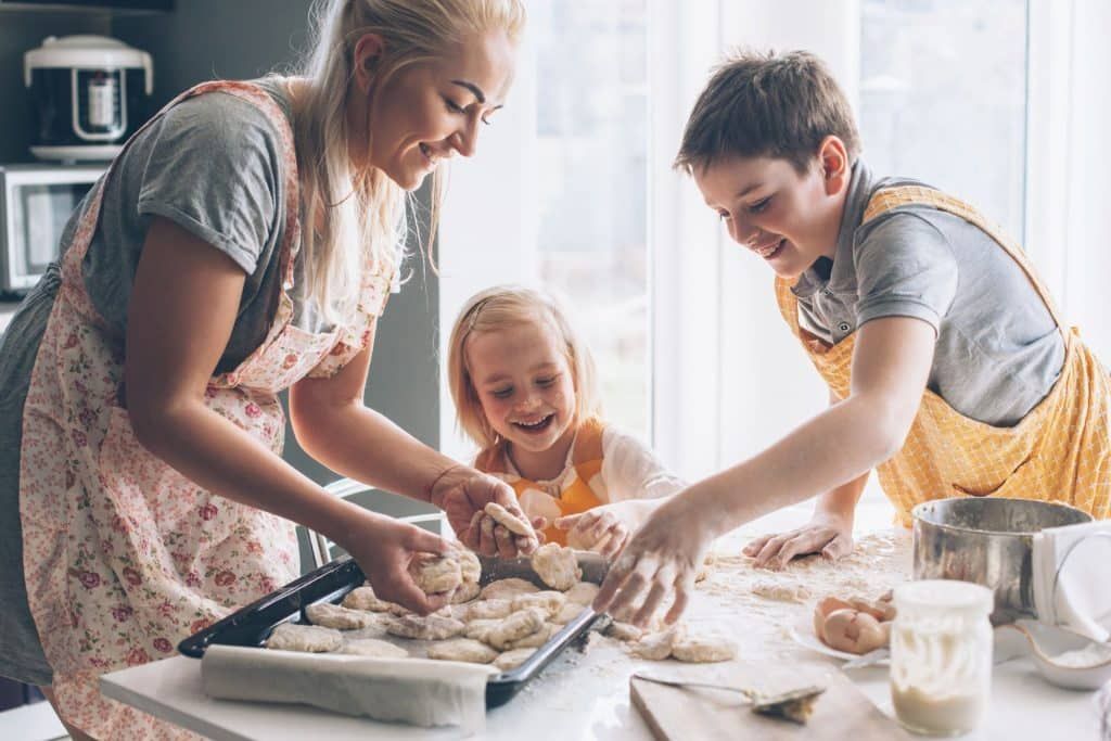 A woman and two children are preparing food in a kitchen.
