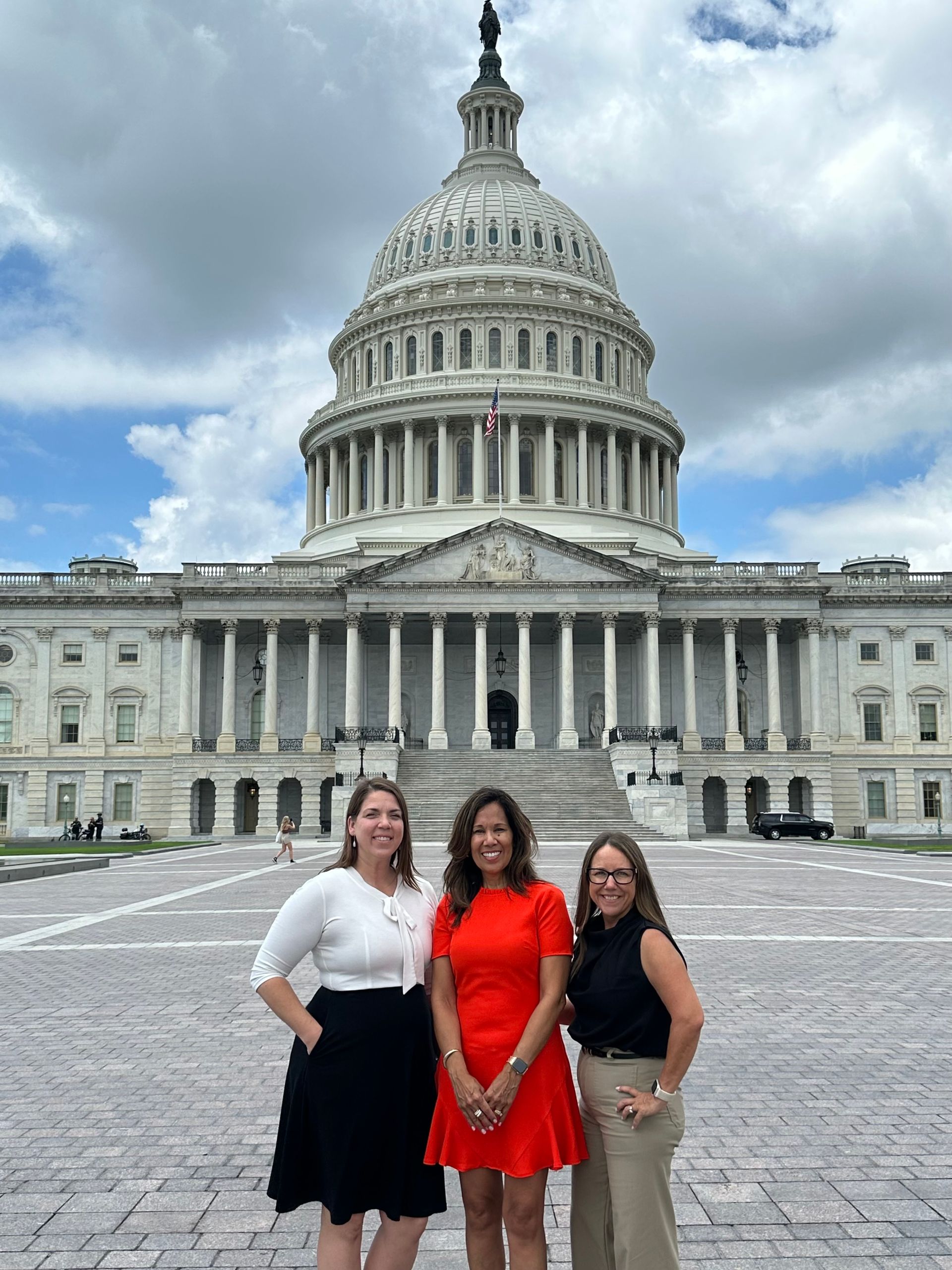Three women in front of the U.S. Capitol Building; one in red dress, one in black skirt, and one in tan pants.