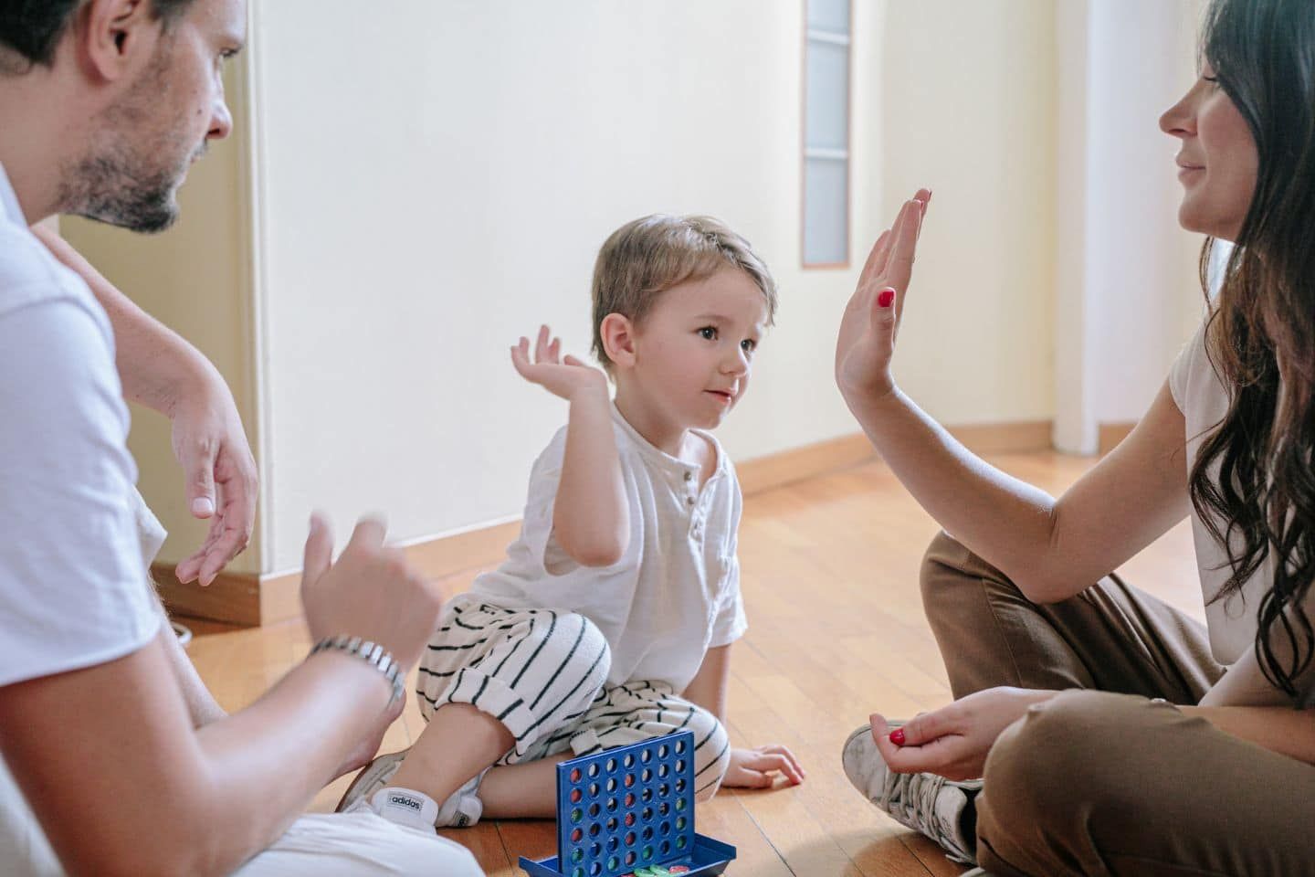 A family is sitting on the floor playing a game and giving each other a high five.