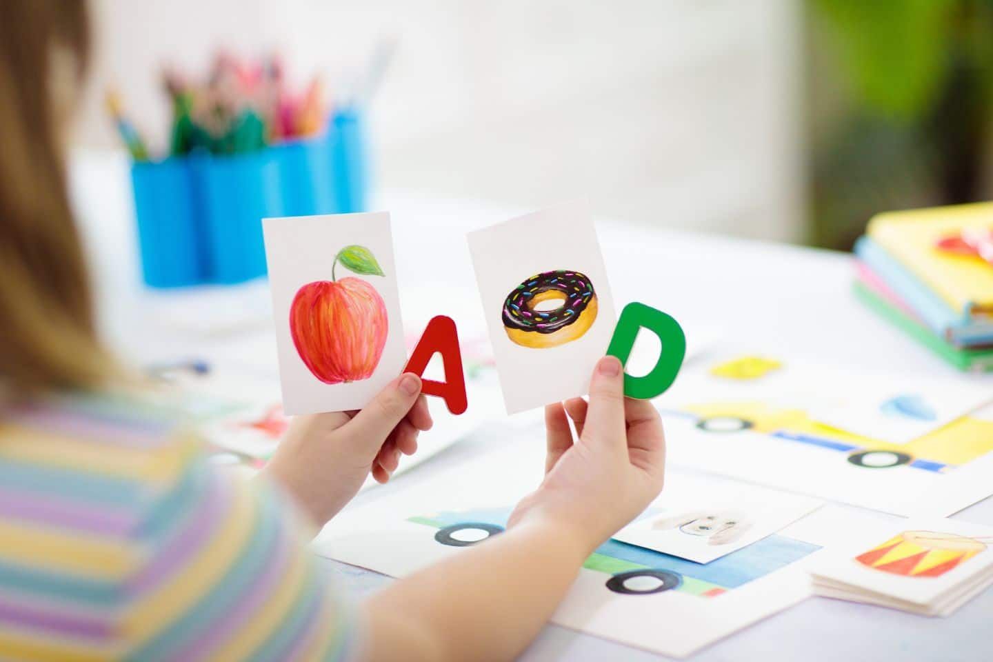 A child is holding a card with the letter a and p on it.