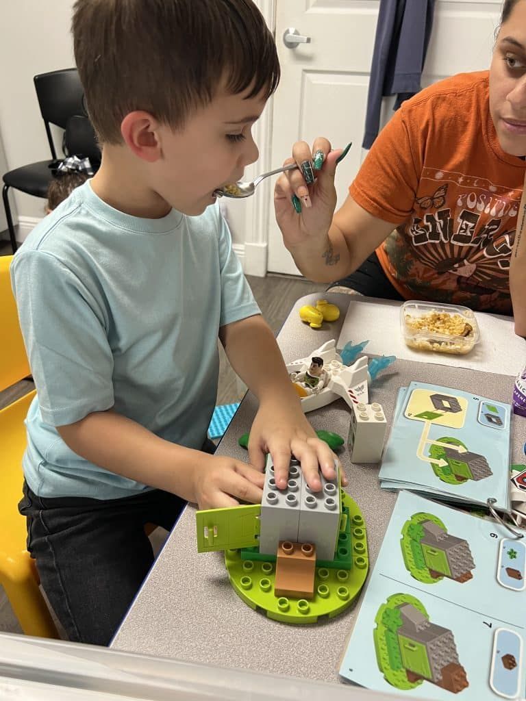 A man and a boy are sitting at a table playing with lego blocks.
