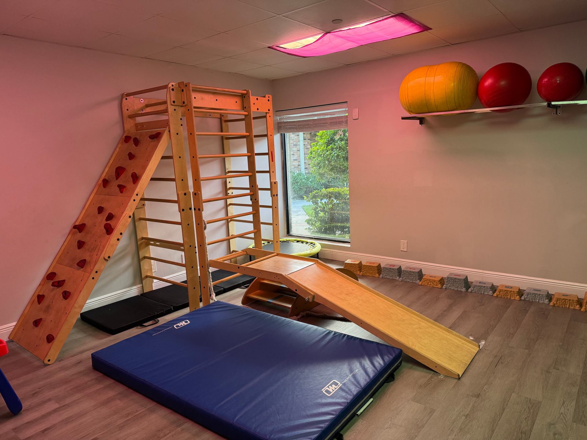 A gym with a climbing wall , a slide , a mat and balls.