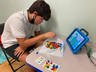 A young boy is sitting at a table playing a game with a tablet.