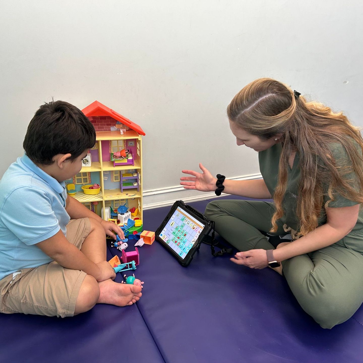 A woman sits on the floor with a child playing with toys and a tablet