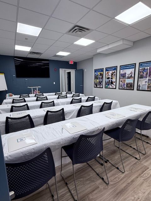 Training room setup with rows of tables, chairs, and presentation screen. Blue and white decor.