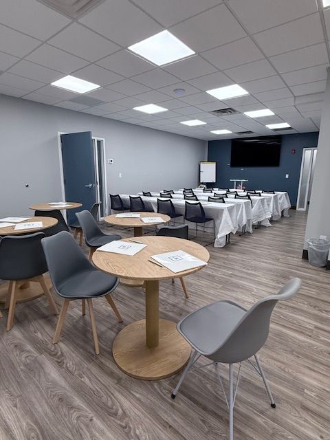 Conference room with round tables and chairs in foreground, rectangular tables and chairs in background.