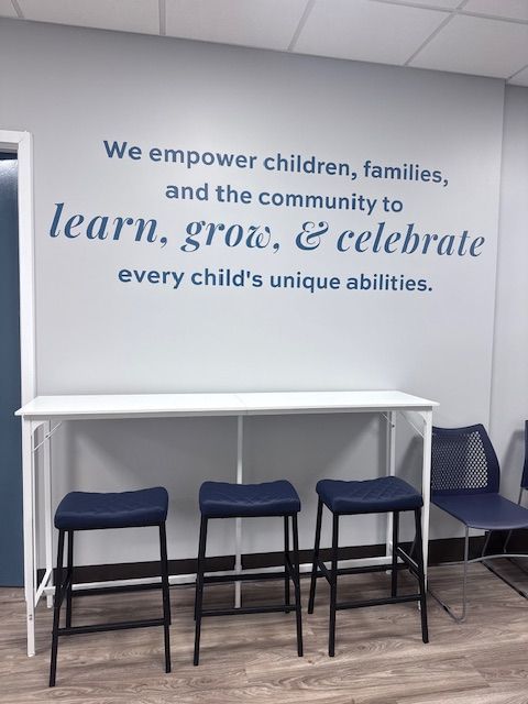 A white table with three blue stools in front of a wall with an inspirational quote.