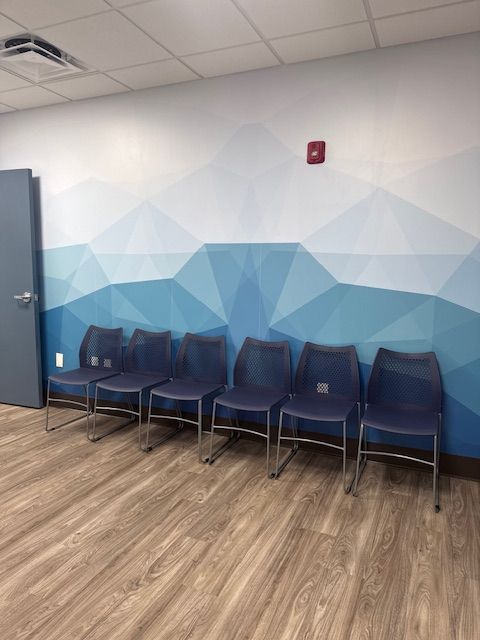 Six blue chairs in a waiting area with a geometric blue and white mural on the wall.