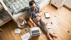 A man is sitting on the floor with a baby and a laptop.