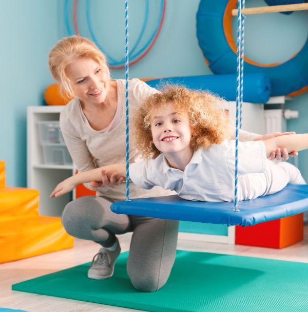 A woman is kneeling next to a child sitting on a swing.