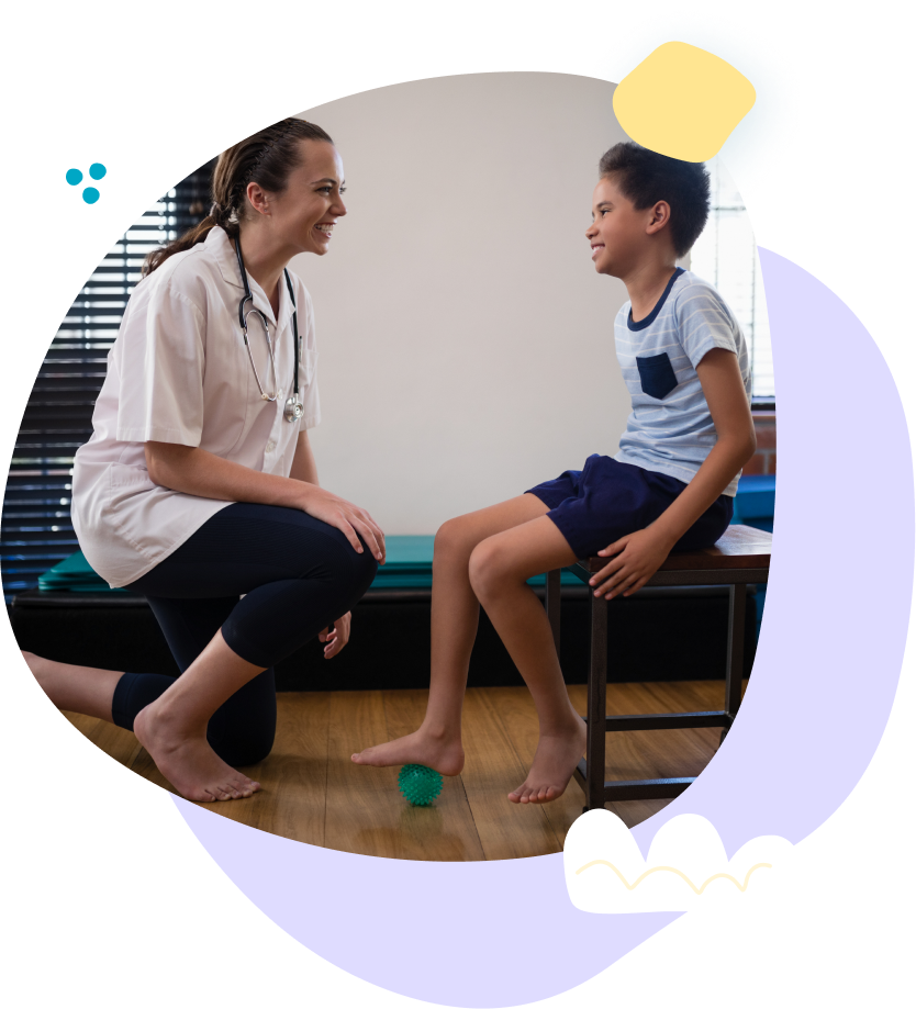 A doctor is kneeling down next to a young boy sitting on a stool.