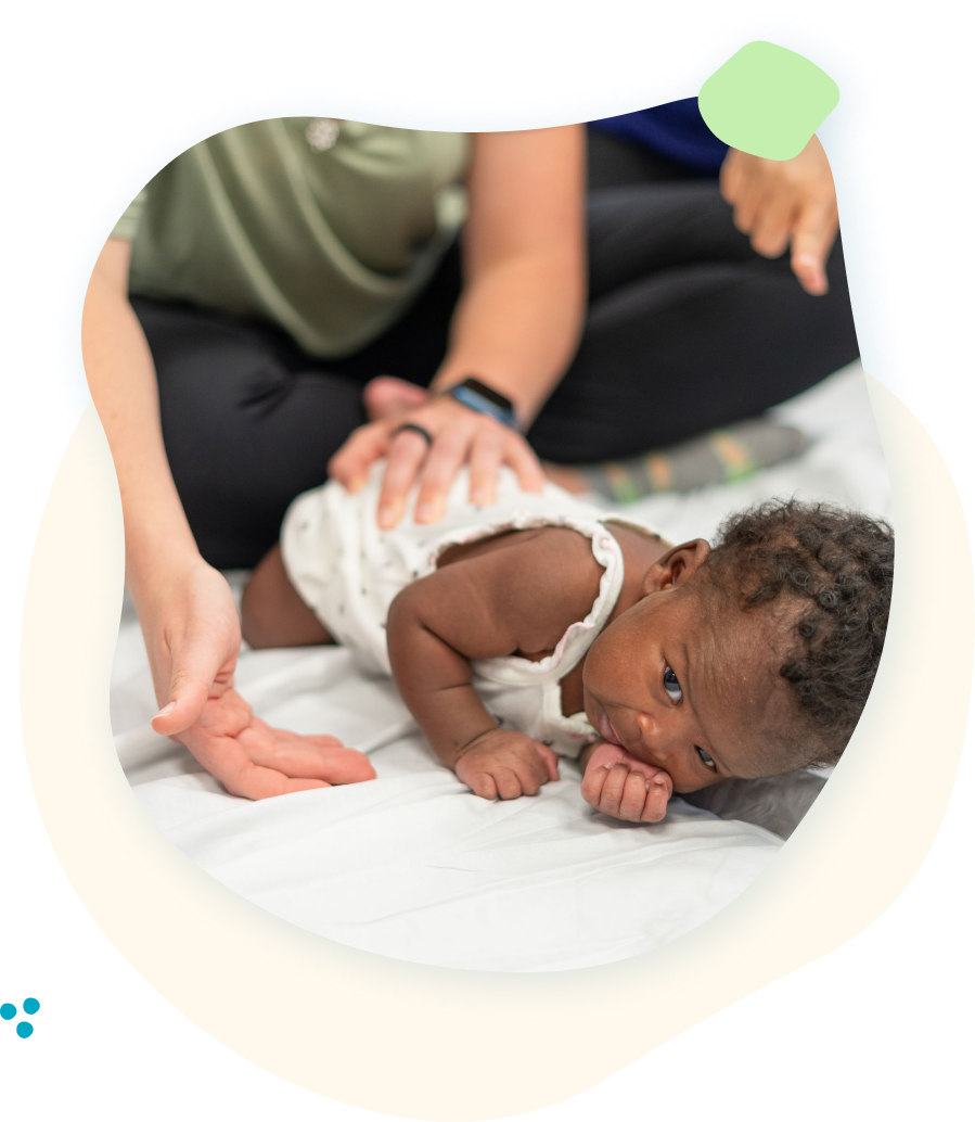 A baby is crawling on the floor while being held by a woman.