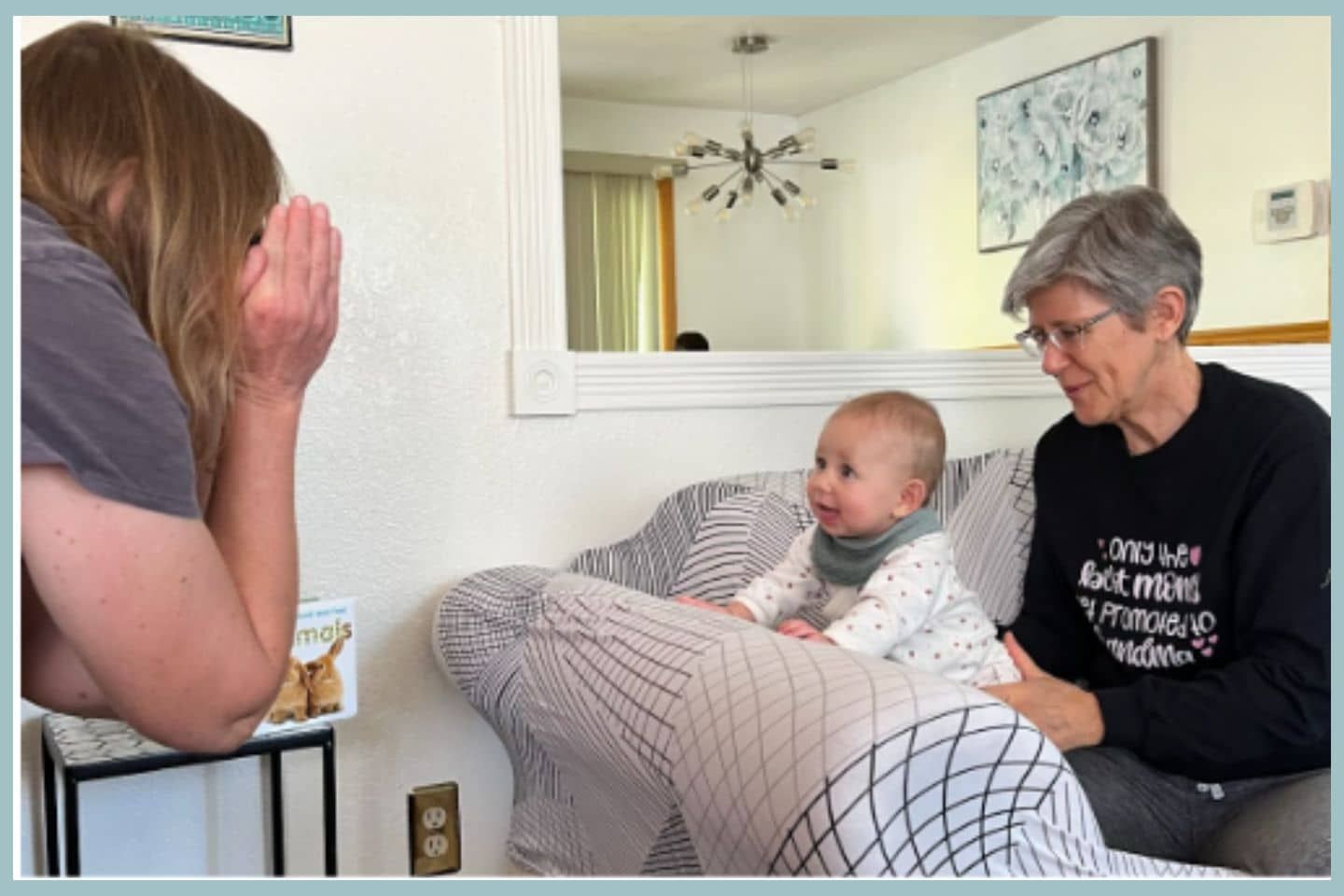 A woman is sitting on a couch holding a baby while another woman looks on.