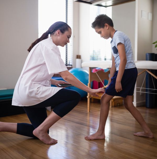 A woman is kneeling down next to a young boy who is standing on a wooden floor