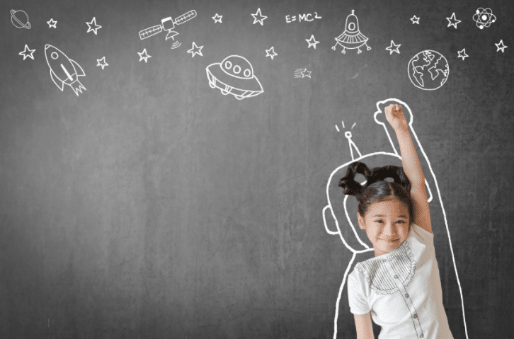 A little girl is standing in front of a blackboard with drawings on it.