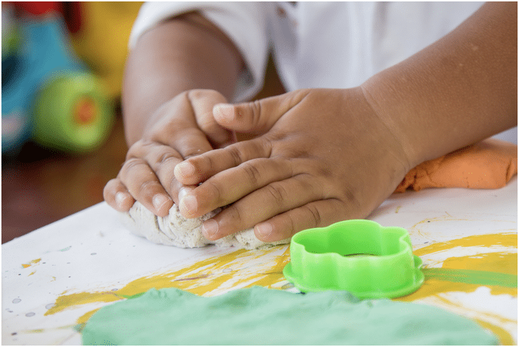 A child is playing with play dough on a table.