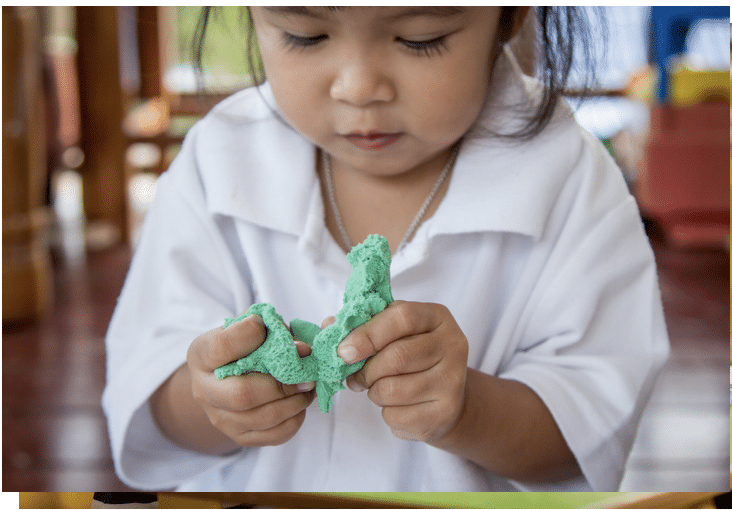 A little girl in a white shirt is playing with kinetic sand.