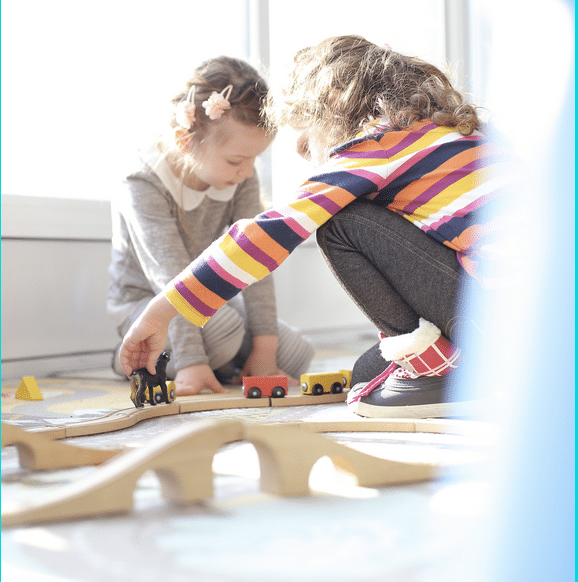 Two little girls are playing with a wooden train set