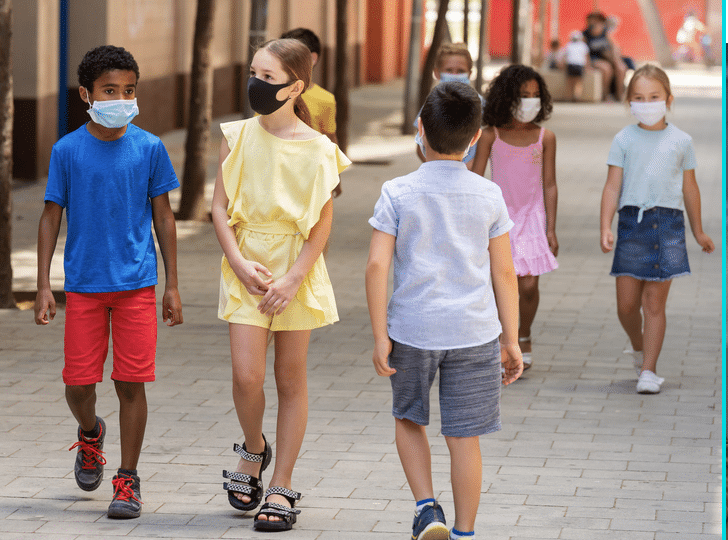 A group of children wearing face masks are walking down a sidewalk.