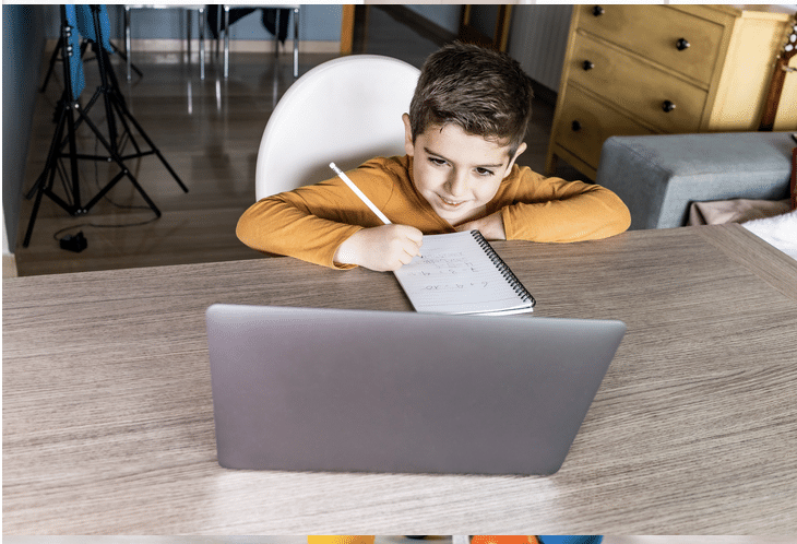 A young boy is sitting at a desk using a laptop computer.