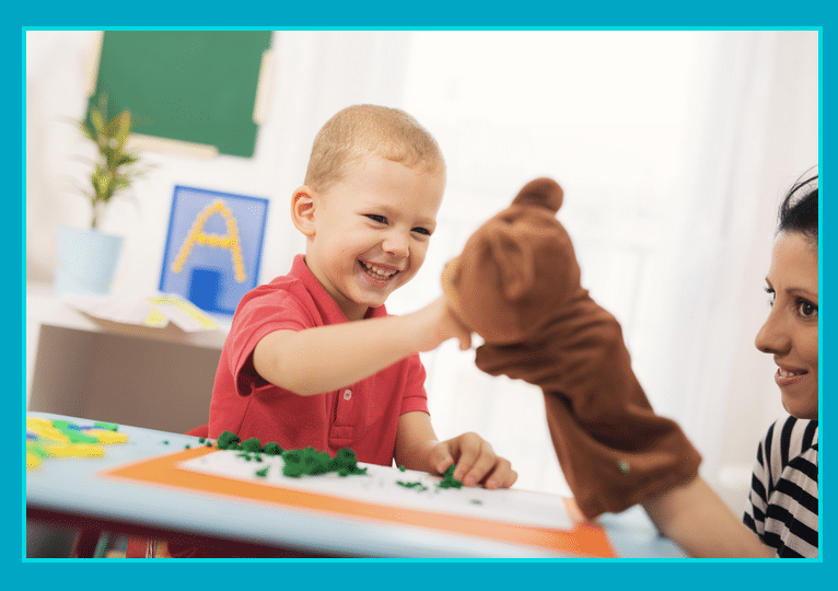 A little boy is playing with a puppet on a table.