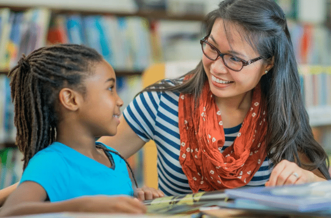 A woman is reading a book to a young girl in a library.