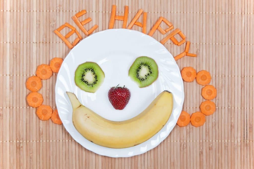 A white plate with a banana kiwi and strawberry on it