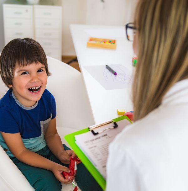 A little boy is sitting in a chair talking to a woman who is holding a clipboard