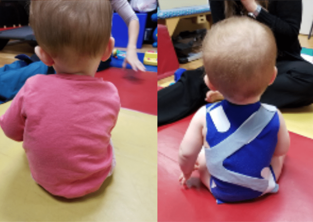 A baby in a pink shirt and a baby in a blue shirt are sitting on the floor