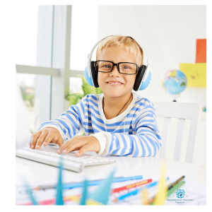 A young boy wearing headphones and glasses is using a computer.