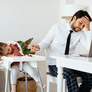 A man is sitting at a table with a laptop and a child in a high chair