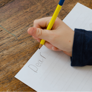 A person is writing a letter with the word dear on it