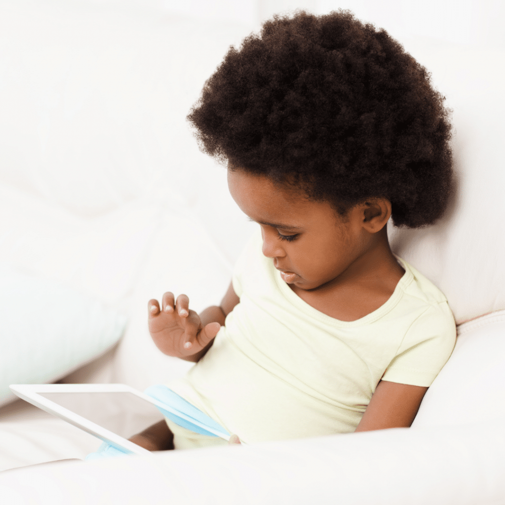 A little girl is sitting on a couch looking at a tablet
